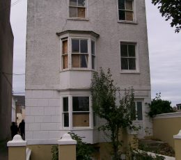 A derelict house with three levels, 2 windows on each row wit a window and door on the first level.