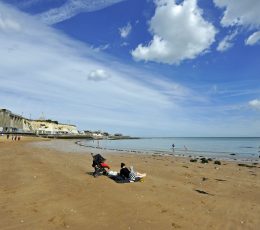 A person with a pushchair sitting on the sandy beach