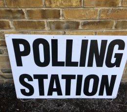 Polling Station - sign written in block caps on white, leaning against a brick wall