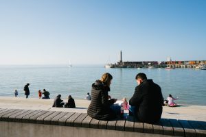 couple eating fish and chips sitting on the step revetment looking out to margate harbour