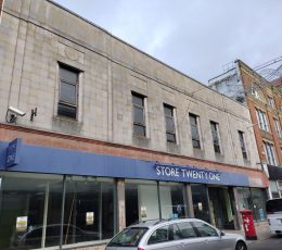Empty glass fronted shop with grey building above with 6 glass windows.
