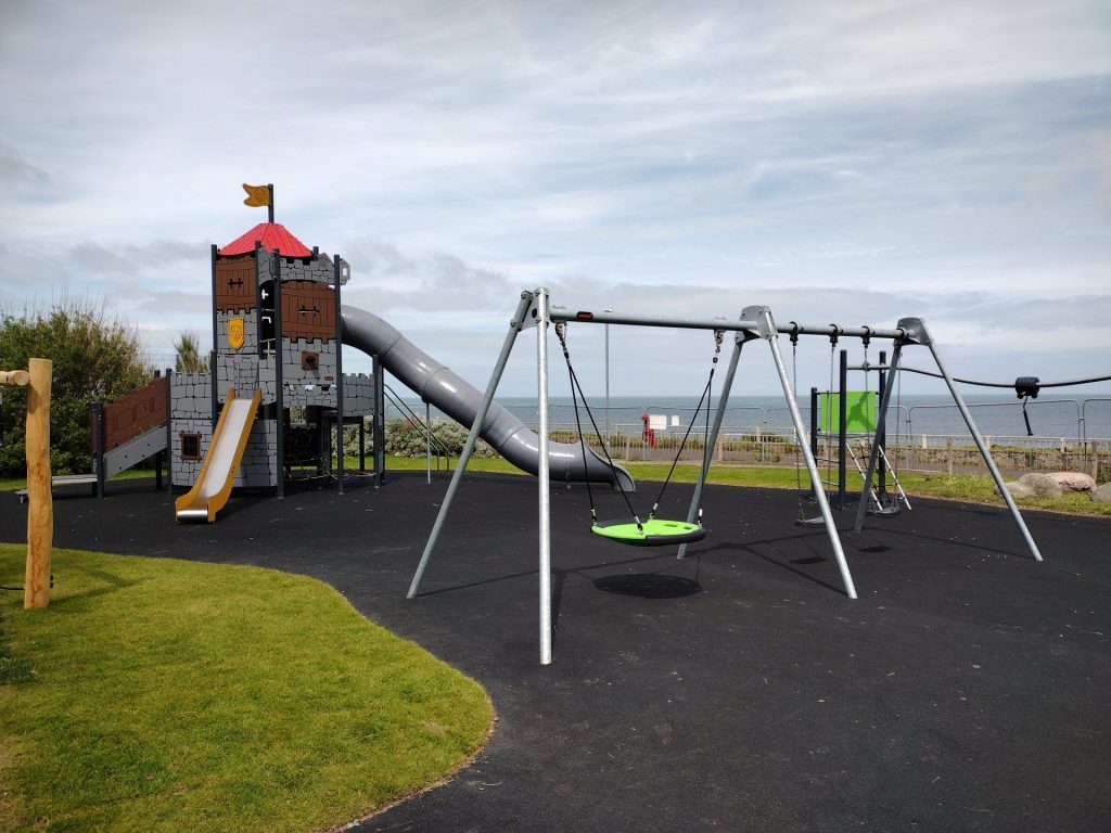 Image of new play equipment which includes a castle play system, and swings