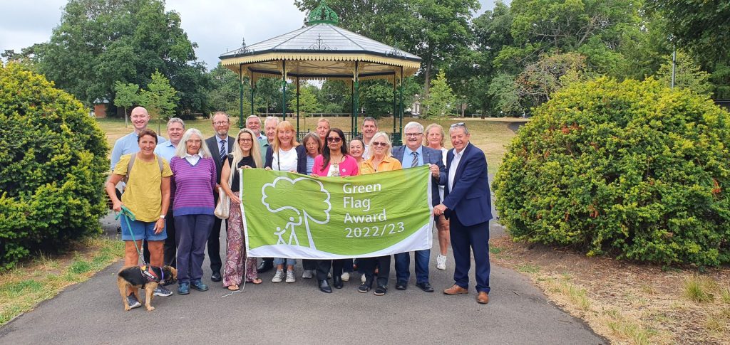image of councillors, council officers and community partners holding the Green Flag in front of Ellington Park bandstand