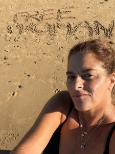 Tracey Emin on the beach with Free Woman written in the sand
