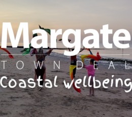 Three women and two children doing bellydance with bright coloured scarfs on the beach at sunset