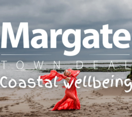 Woman wearing bright orange draping clothes and meditating on beach in front of the sea and in between cliff stacks