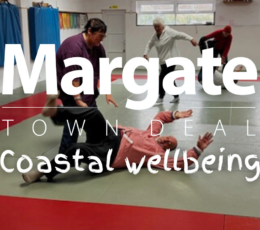 Five adults, men and women inside a martial arts centre practicing self defence moves with one man having been tackled to the floor.