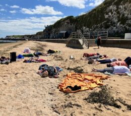 Group of people lying on the beach meditating below chalk cliffs in the sun