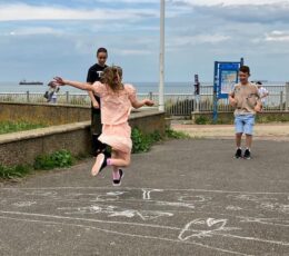 Thanet Parkour coach, coaching young girl to do a parkour jump over chalk drawn lines on the upper promenade