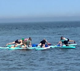 Group of people in a circle practicing yoga on stand up paddleboards on the sea