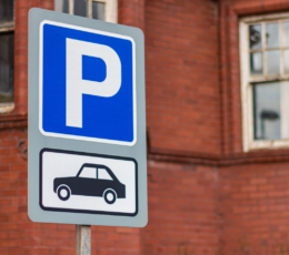 Parking sign, capital P in white on a bright blue background, with an illustration of a car underneath in black on a white background
