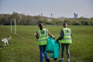 Litter pickers with CleanUP UK hi-vis vests, holding litter bags, walking across a field.
