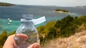 Plastic bottle with cap tie, held against coastal backdrop.