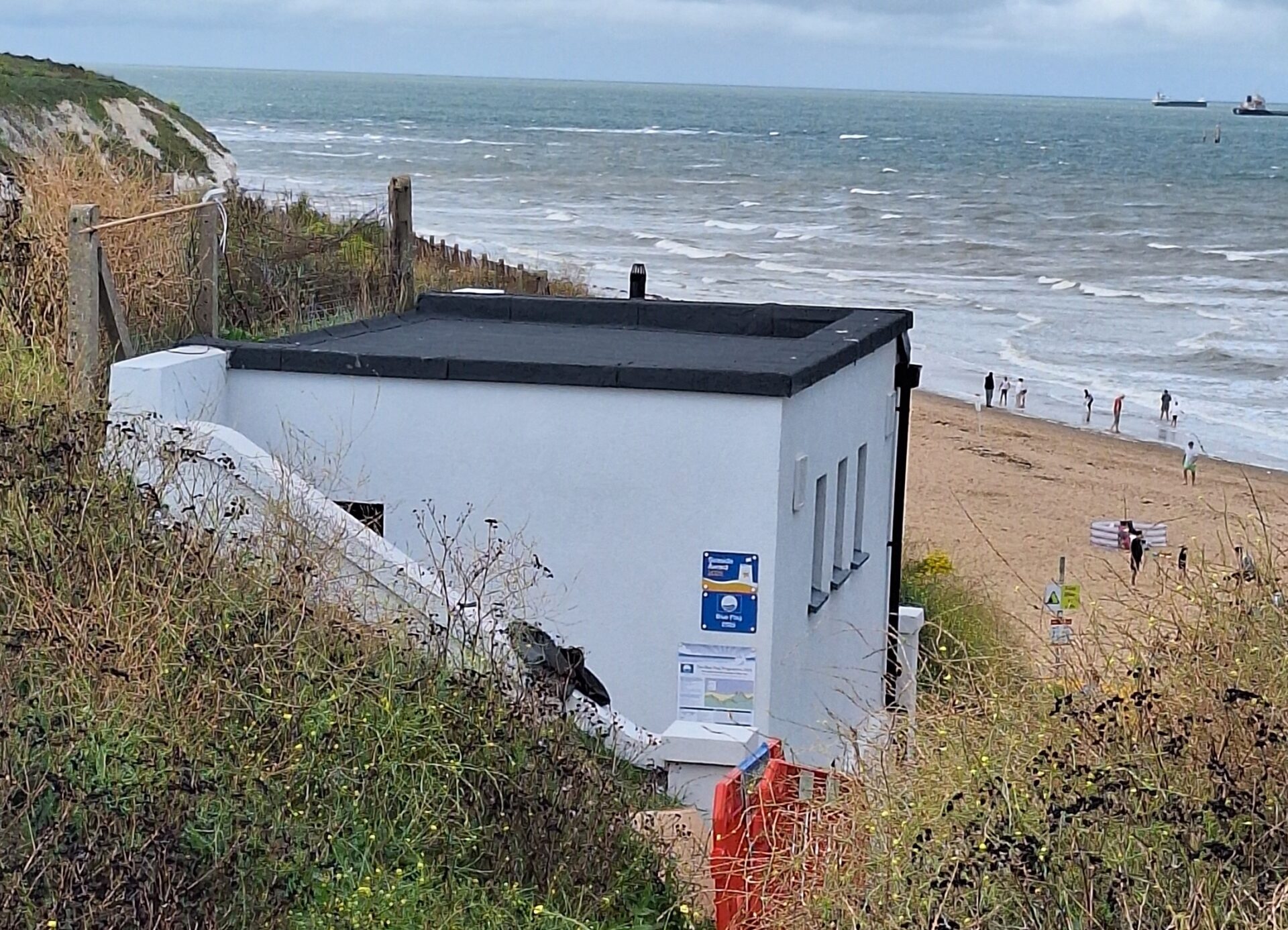 Exterior of toilet block at Botany Bay in Broadstairs. Beach and sea in the background, with people enjoying the coast.
