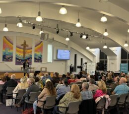 People sitting in rows in the Queens Road Baptist Church auditorium, with a speaker at the front