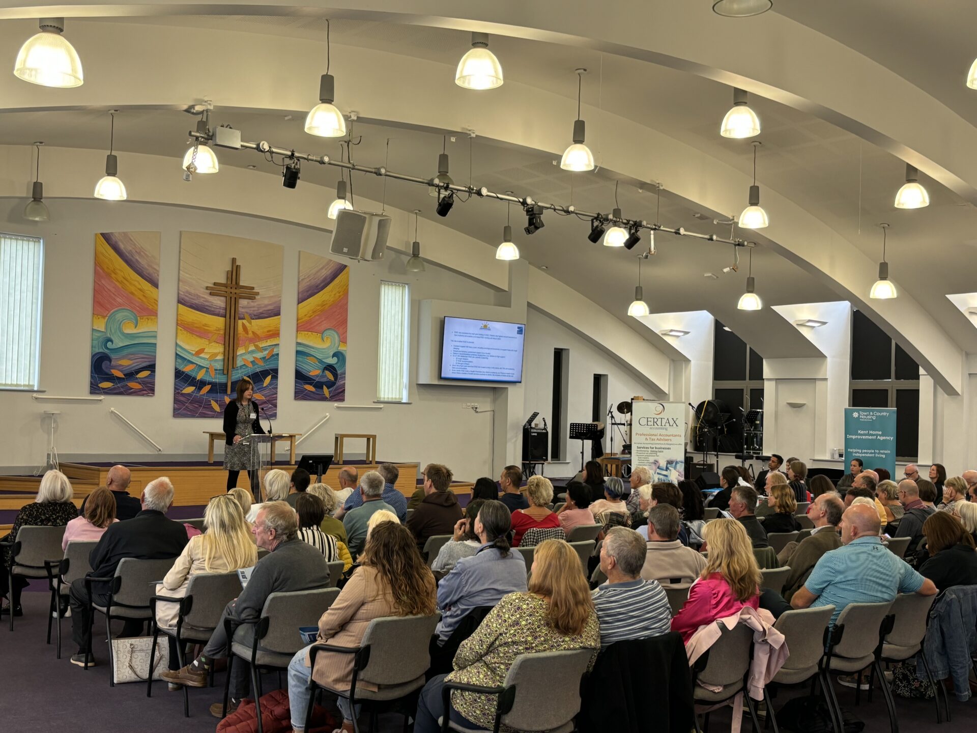 People sitting in rows in the Queens Road Baptist Church auditorium, with a speaker at the front