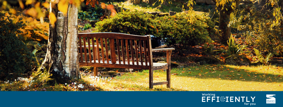 A wooden memorial bench next to a tree in a sunlit park with autumn leaves. A blue banner at the bottom features the Thanet District Council logo and the slogan 'Working efficiently for you'