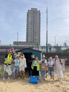 A group of people (some dressed as seagulls) on Margate Main Sands with Arlington House behind them, as part of the Seagull Beach Clean with Rise Up Clean Up Margate CIC