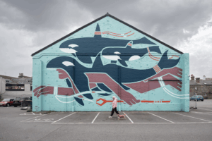 A mural on the side of a building showing a swimming figure alongside whale like creatures.