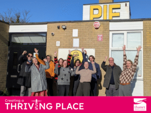 A group of ten people cheer with arms raised outside a brick building featuring a large yellow PIE sign.