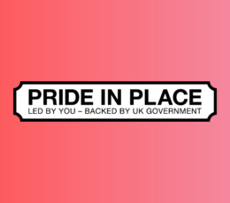 White street sign on a pink background reading: PRIDE IN PLACE. LED BY YOU – BACKED BY UK GOVERNMENT.