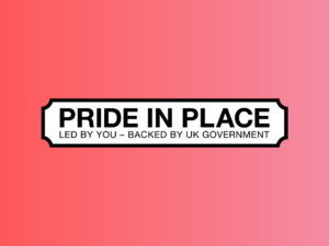 White street sign on a pink background reading: PRIDE IN PLACE. LED BY YOU – BACKED BY UK GOVERNMENT.