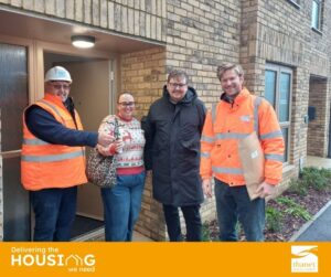 A construction worker hands keys to a smiling couple outside a new brick home. All four people are smiling.