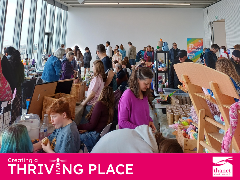 A bustling indoor market filled with people browsing stalls of handmade crafts, crochet items, and baked goods.