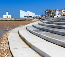 Wide, curving concrete sea steps lead down to a sandy beach in Margate, with modern and historic buildings behind.