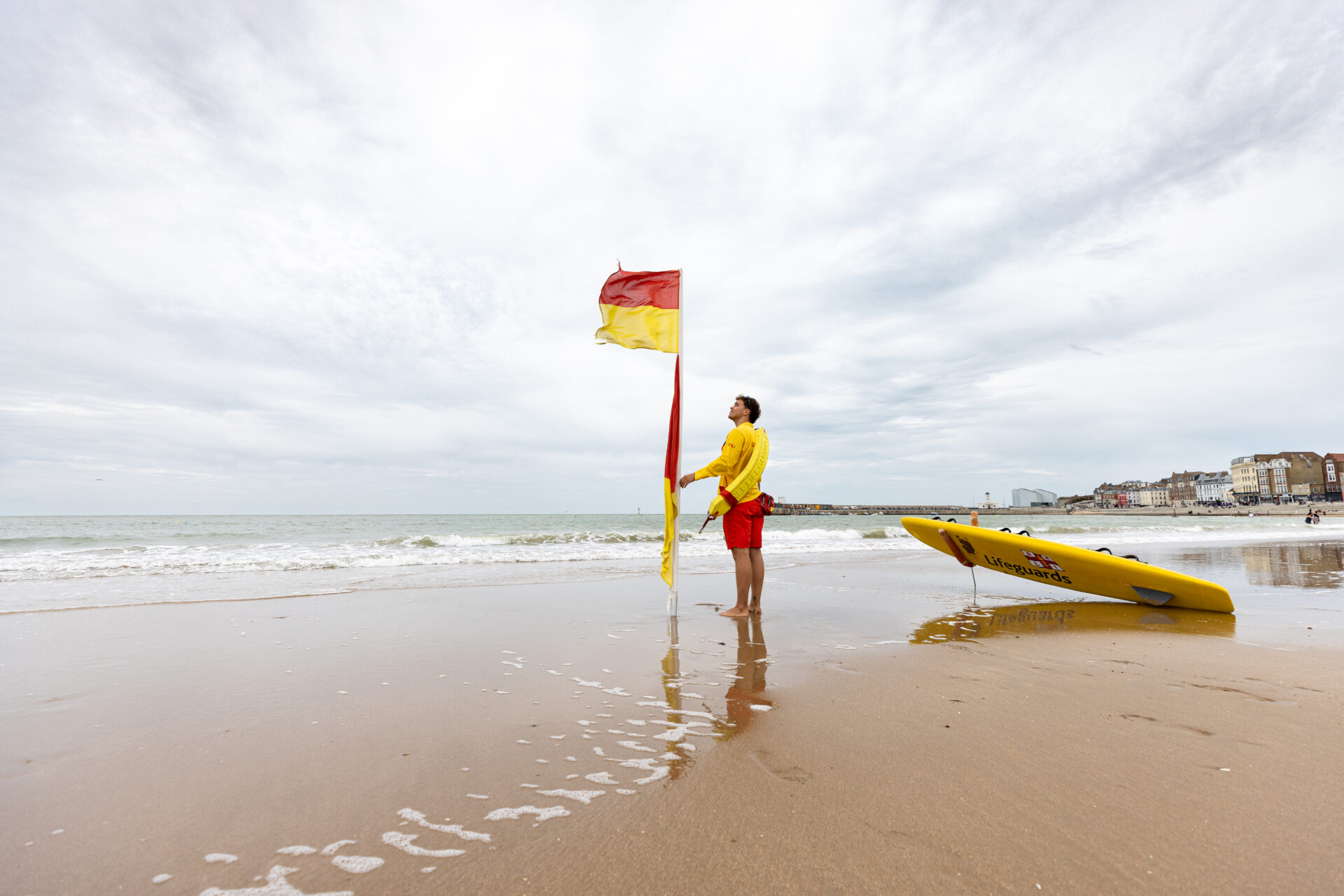 RNLI Senior lifeguard moving a red and yellow flag at Margate Main Sands, Kent.