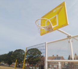 Low-angle view of a bright yellow basketball backboard and hoop attached to a white metal cage frame.