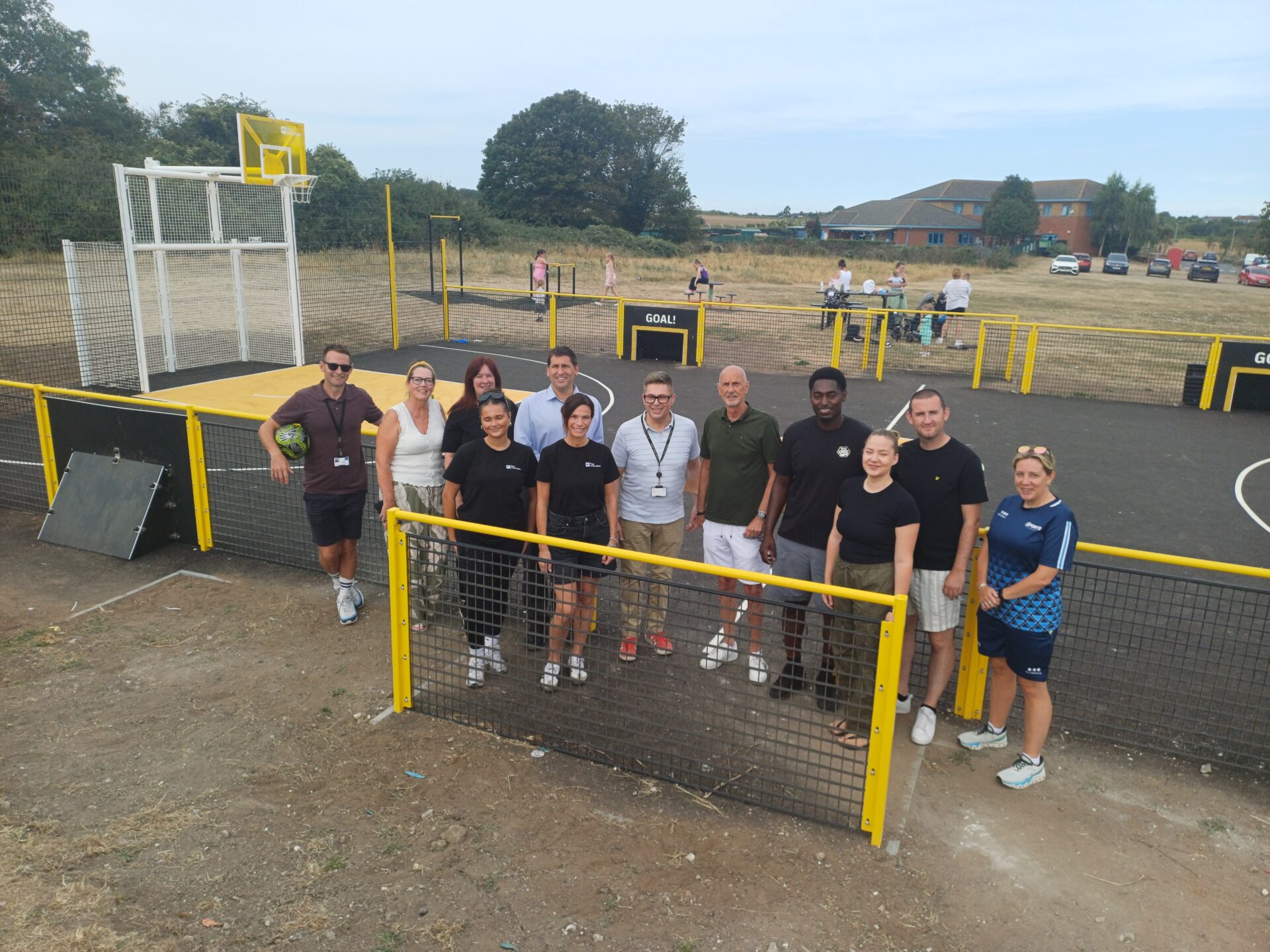 A group of eleven people pose together for a photo behind a low yellow fence at a sports court.