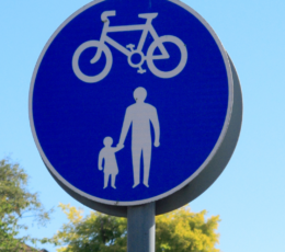 A circular blue road sign showing white symbols of a bicycle above an adult holding hands with a child.