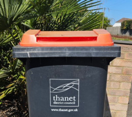 Black wheelie bin with a red lid. Printed white logo and text read Thanet District Council and www.thanet.gov.uk