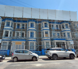 Exterior of a grand multi-storey building covered in full-height scaffolding and safety netting during restoration.